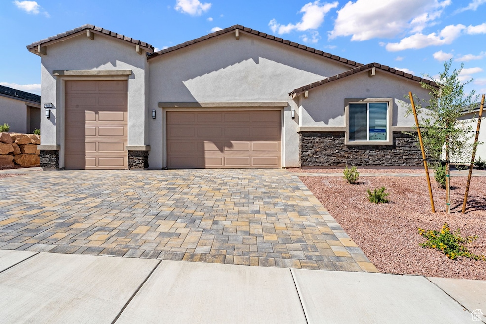 Mediterranean / spanish-style house featuring a garage, decorative driveway, stone siding, stucco siding, and a tile roof