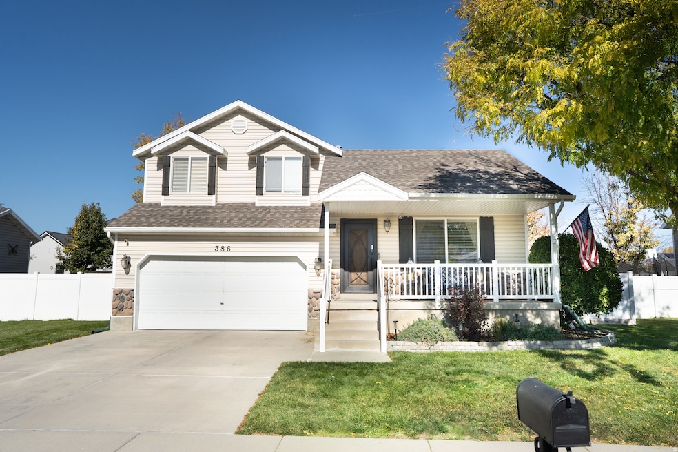 Tri-level home with covered porch, driveway, an attached garage, roof with shingles, and stone siding