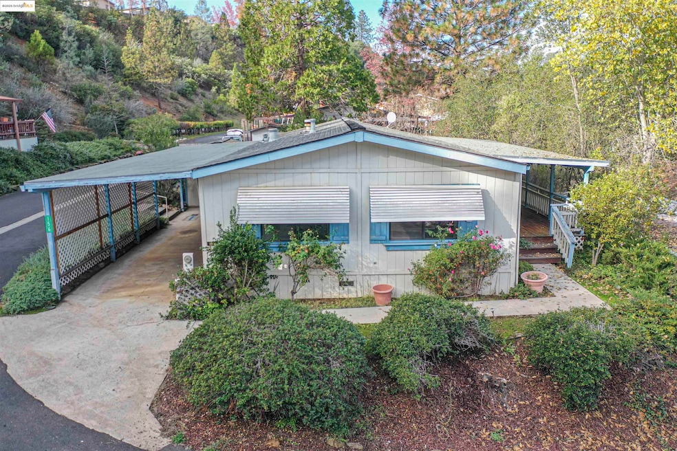 View of front of home featuring an attached carport, concrete driveway, and view of wooded area