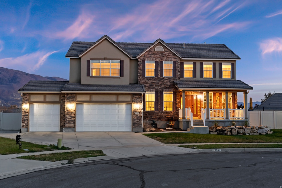 View of front of property with stone siding, driveway, covered porch, an attached garage, and a tiled roof