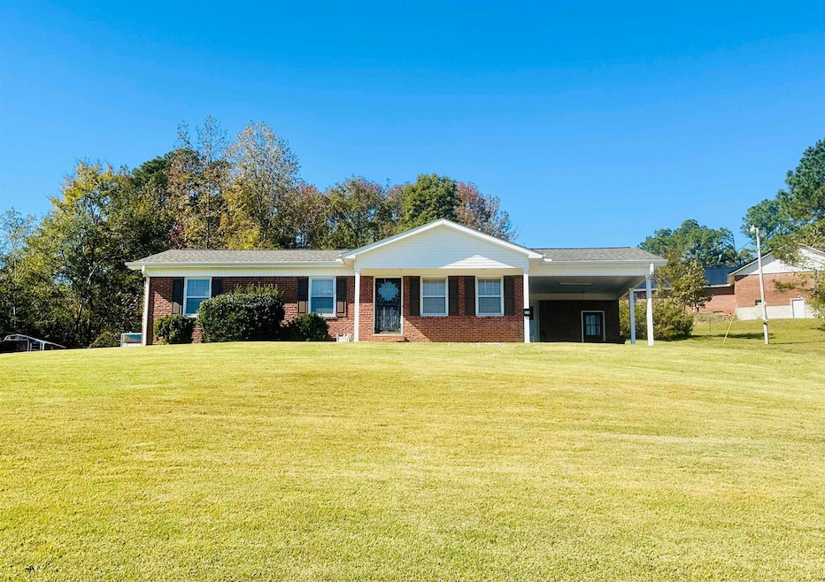 Single story home with a front yard, an attached carport, brick siding, and covered porch