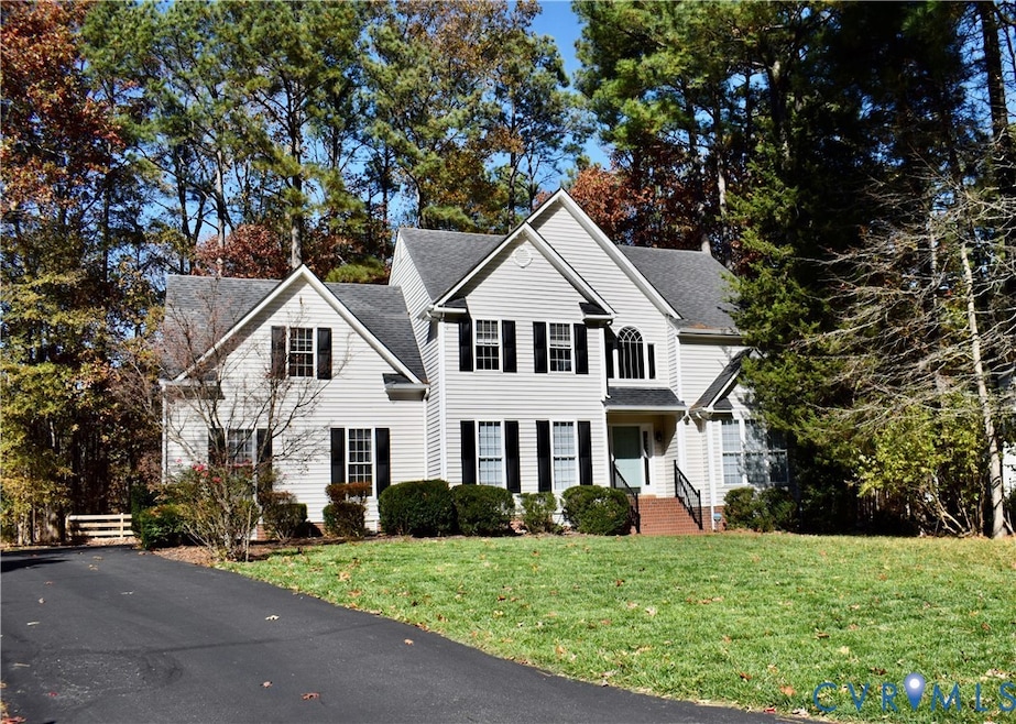 Traditional home with a shingled roof, a front yard, and view of wooded area
