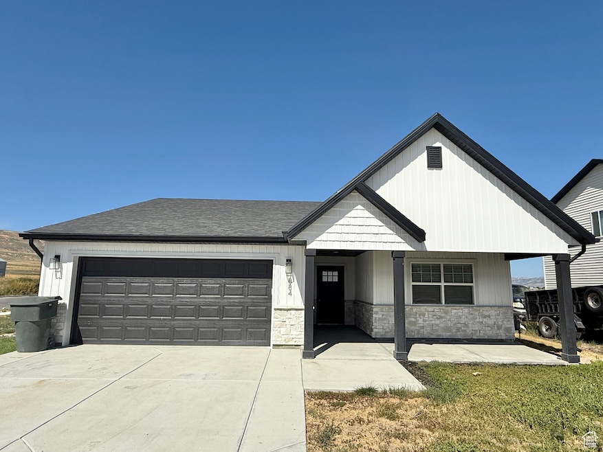 View of front of property with an attached garage, stone siding, a porch, driveway, and a shingled roof