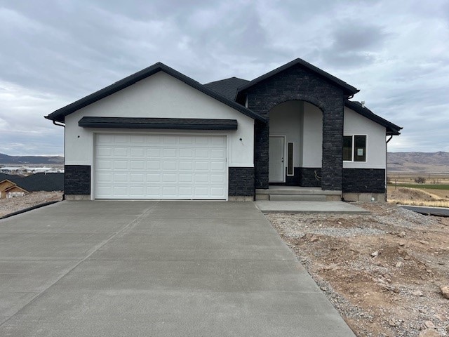 View of front of house featuring stucco siding, stone siding, concrete driveway, a garage, and a mountain view