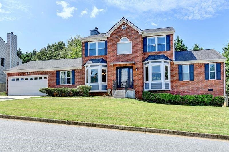 Colonial home with a chimney, brick siding, driveway, and a front lawn