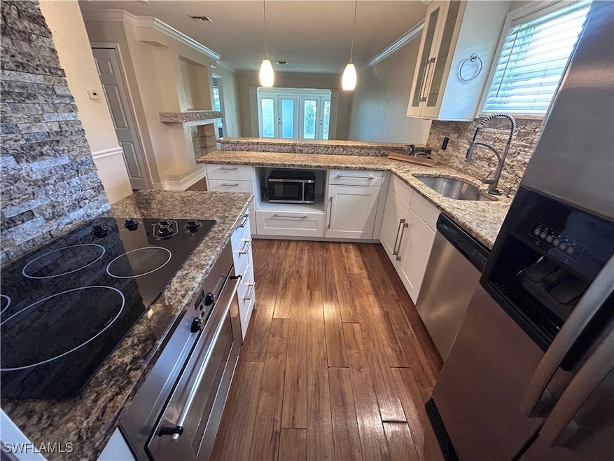 Kitchen featuring stainless steel appliances, light stone counters, dark wood-type flooring, glass insert cabinets, and white cabinetry