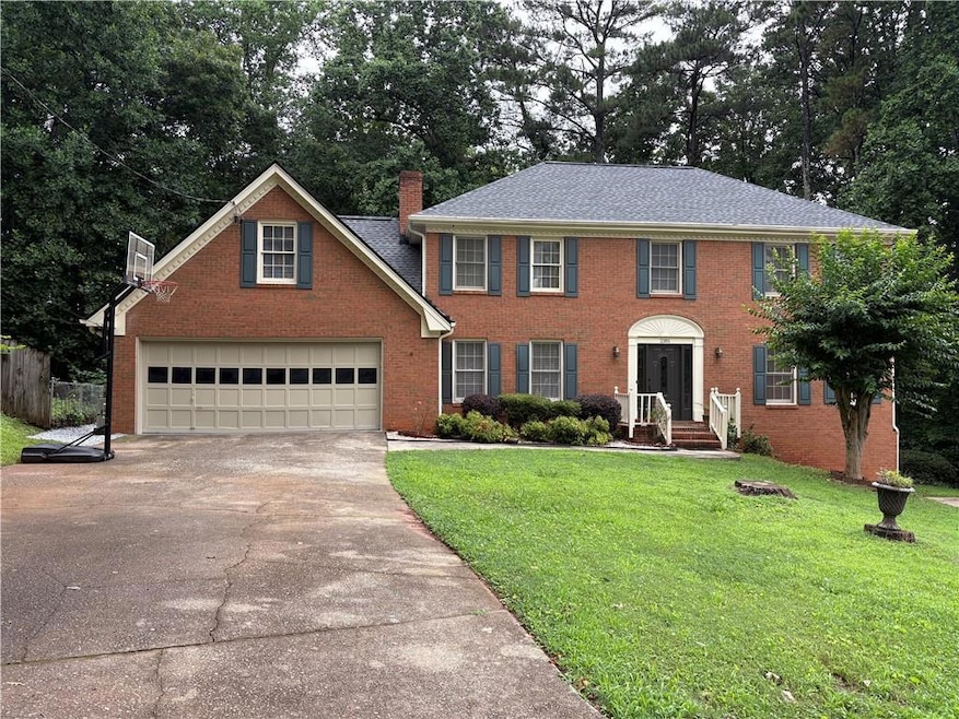 Colonial house with concrete driveway, a chimney, and brick siding