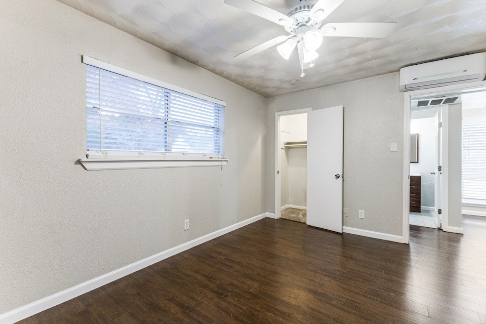 Unfurnished bedroom featuring dark wood-type flooring, a wall mounted air conditioner, a walk in closet, a ceiling fan, and a textured wall