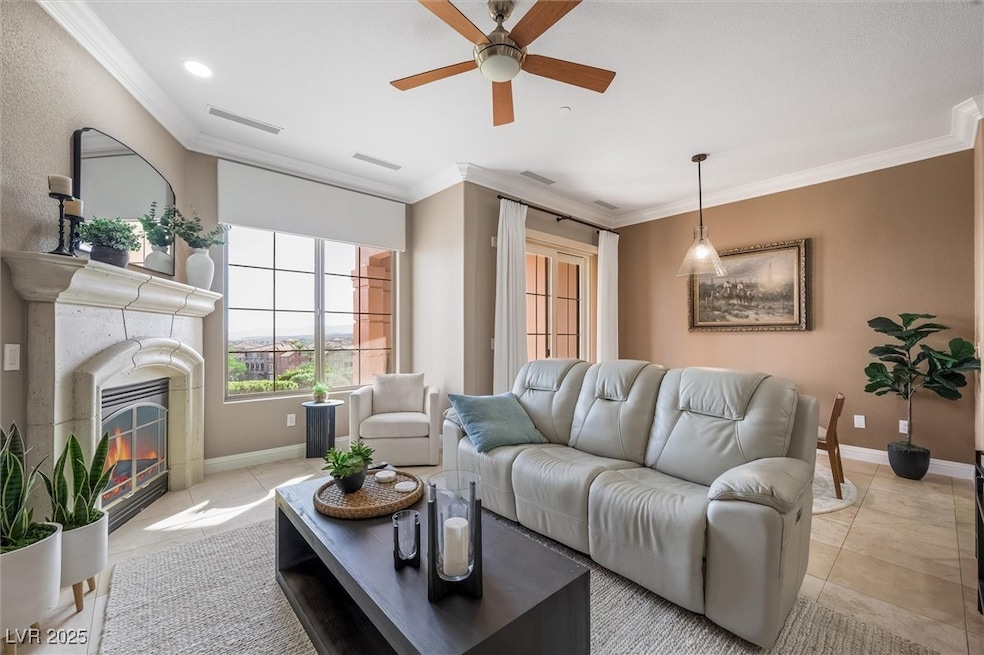 Living area with ornamental molding, light tile patterned floors, a ceiling fan, and a glass covered fireplace