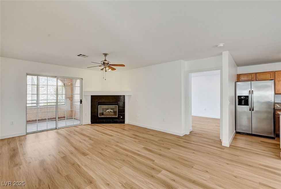 Unfurnished living room featuring a tiled fireplace, light wood-style flooring, and a ceiling fan
