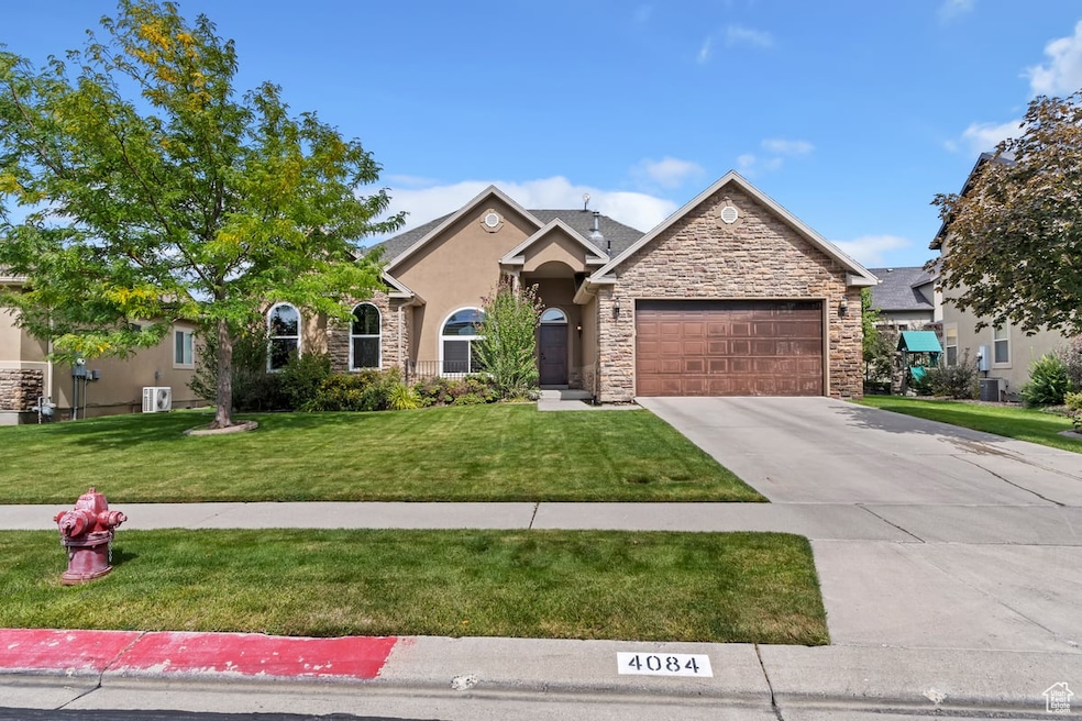 View of front of property with a front lawn, concrete driveway, stone siding, a garage, and stucco siding