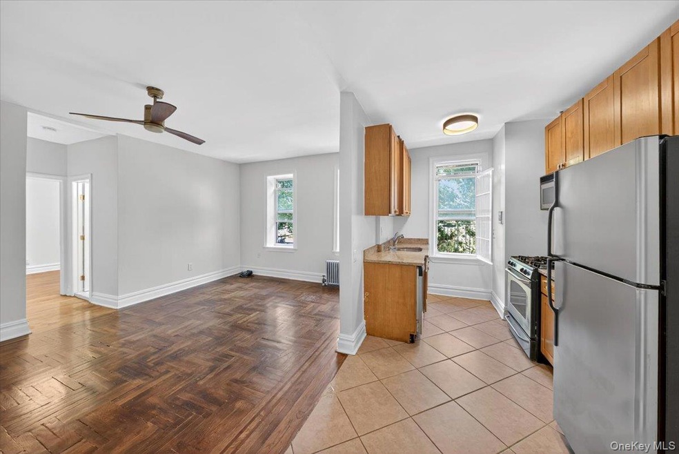 Kitchen with appliances with stainless steel finishes, radiator, a ceiling fan, brown cabinetry, and light stone countertops