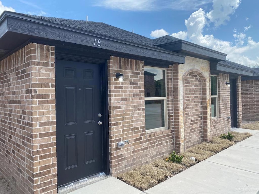 Doorway to property featuring brick siding and a shingled roof