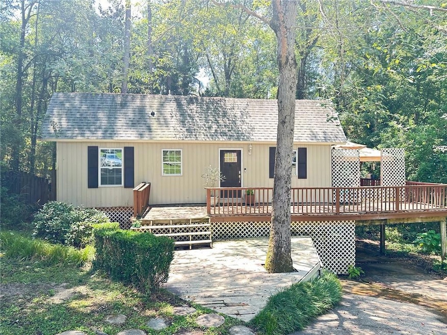 View of front facade featuring a deck, a patio area, a carport, and roof with shingles