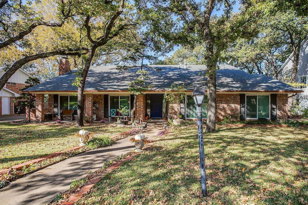 Single story home featuring covered porch, brick siding, a chimney, a shingled roof, and a front yard
