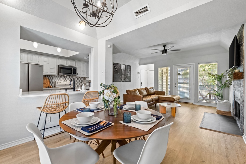 Dining space with light wood-style flooring, a ceiling fan, a fireplace with flush hearth, and a chandelier