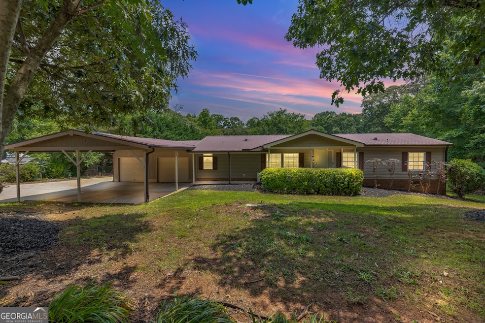 Front of house featuring a garage, carport, yard, and metal roof.