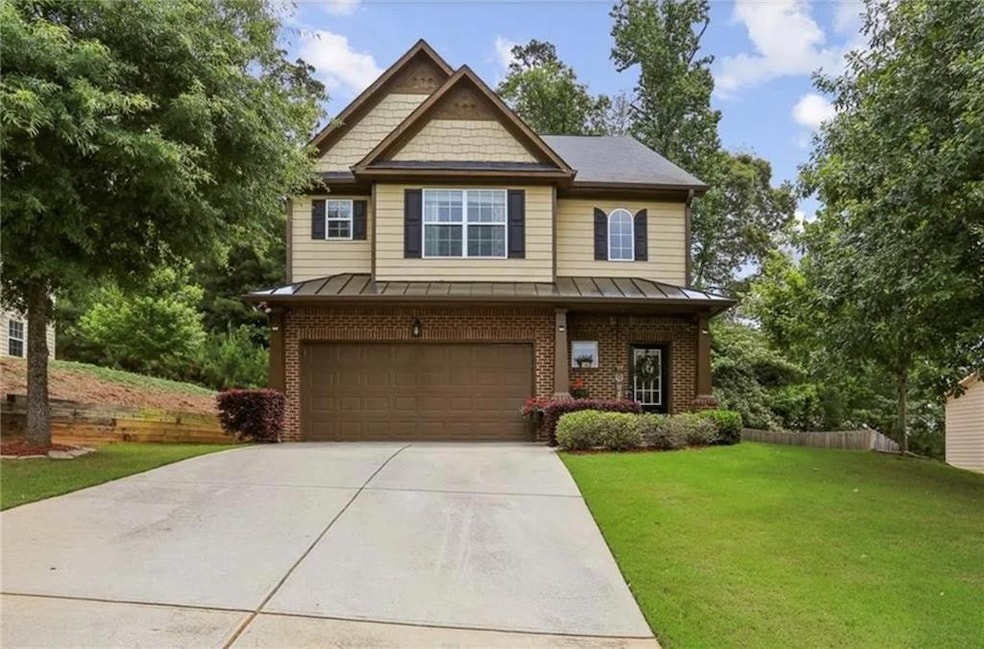 Craftsman-style home featuring an attached garage, a front yard, driveway, brick siding, and a standing seam roof