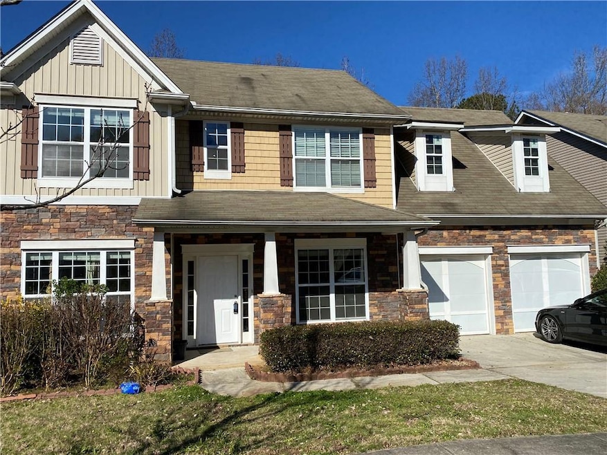 Townhome / multi-family property featuring stone siding, driveway, board and batten siding, and roof with shingles