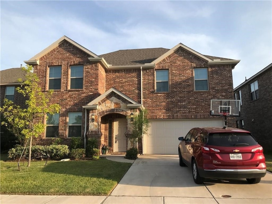 Traditional-style house with brick siding, concrete driveway, a front yard, a garage, and roof with shingles