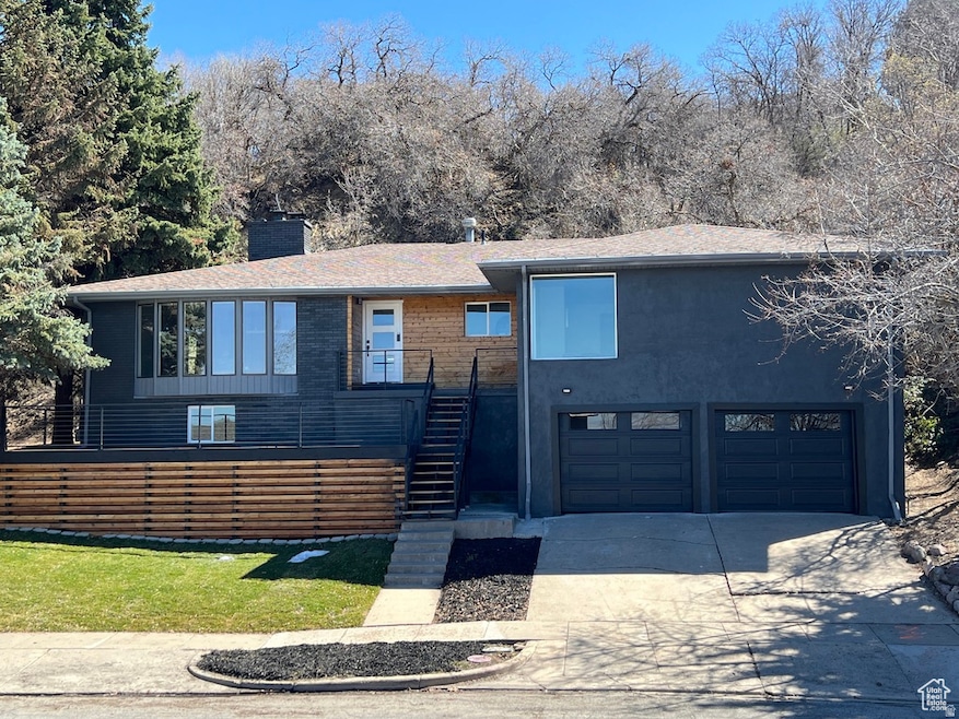 View of front facade featuring stairway, concrete driveway, a chimney, a front yard, and an attached garage