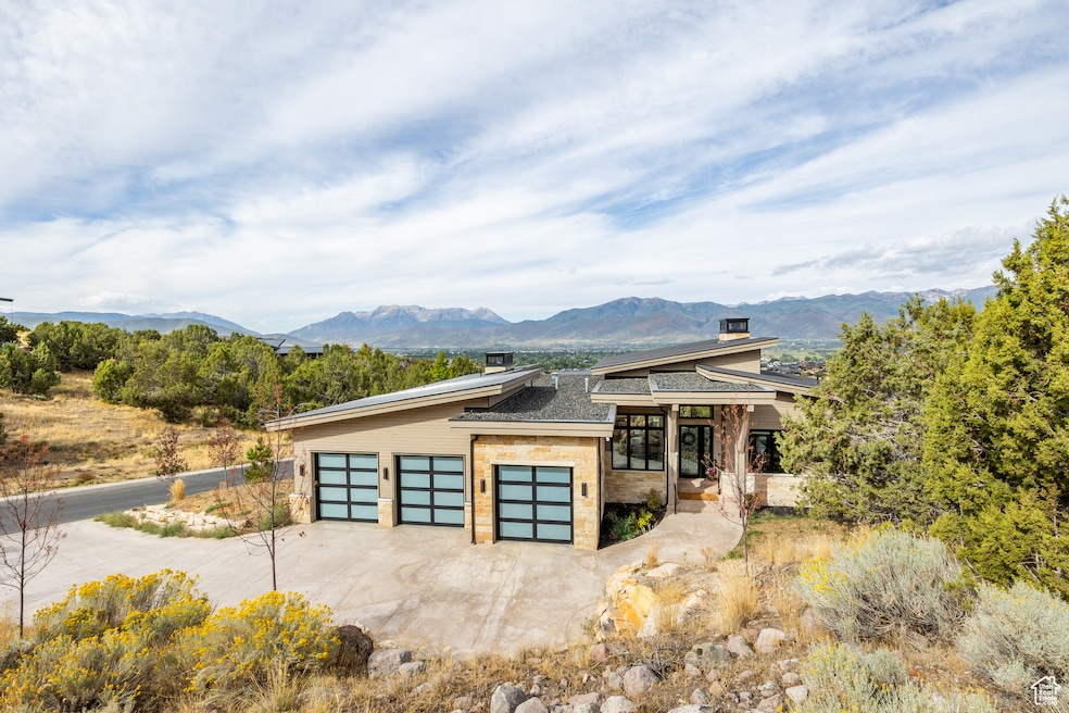 View of front facade featuring stone siding, a mountain view, driveway, a garage, and a chimney