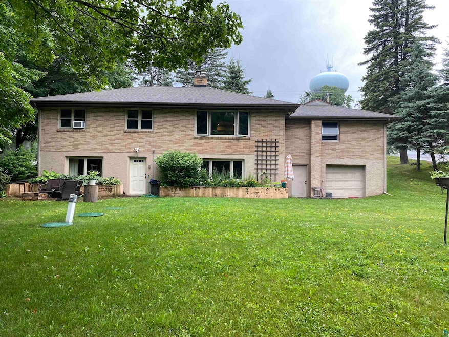 Rear view of house featuring brick siding, an attached garage, a chimney, and a lawn