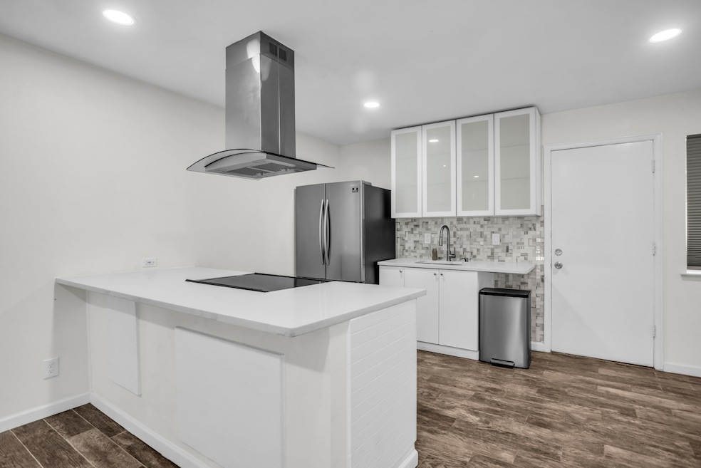 Kitchen featuring dark wood finished floors, decorative backsplash, a peninsula, white cabinets, and glass insert cabinets