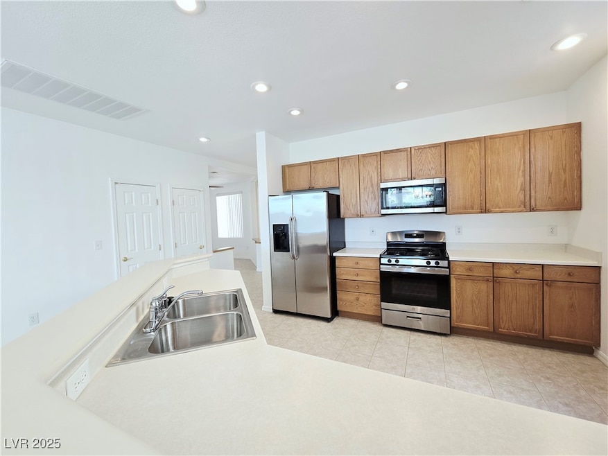 Kitchen featuring stainless steel appliances, brown cabinetry, light countertops, recessed lighting, and light tile patterned floors