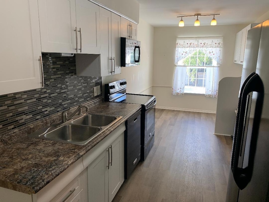Kitchen with black appliances, white cabinetry, si