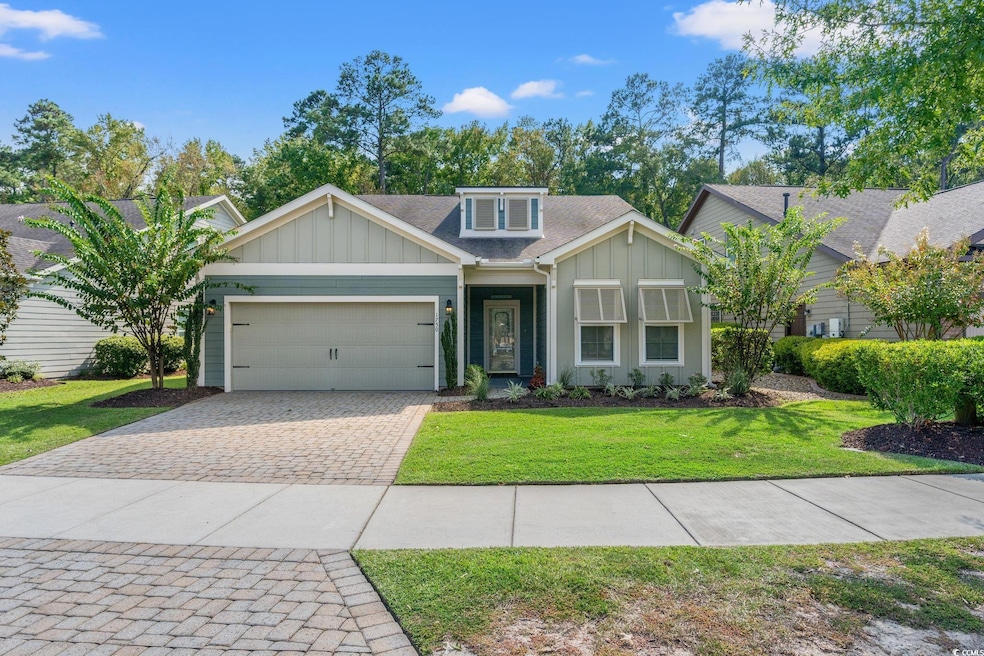 View of front of property with board and batten siding, roof with shingles, decorative driveway, and a front yard