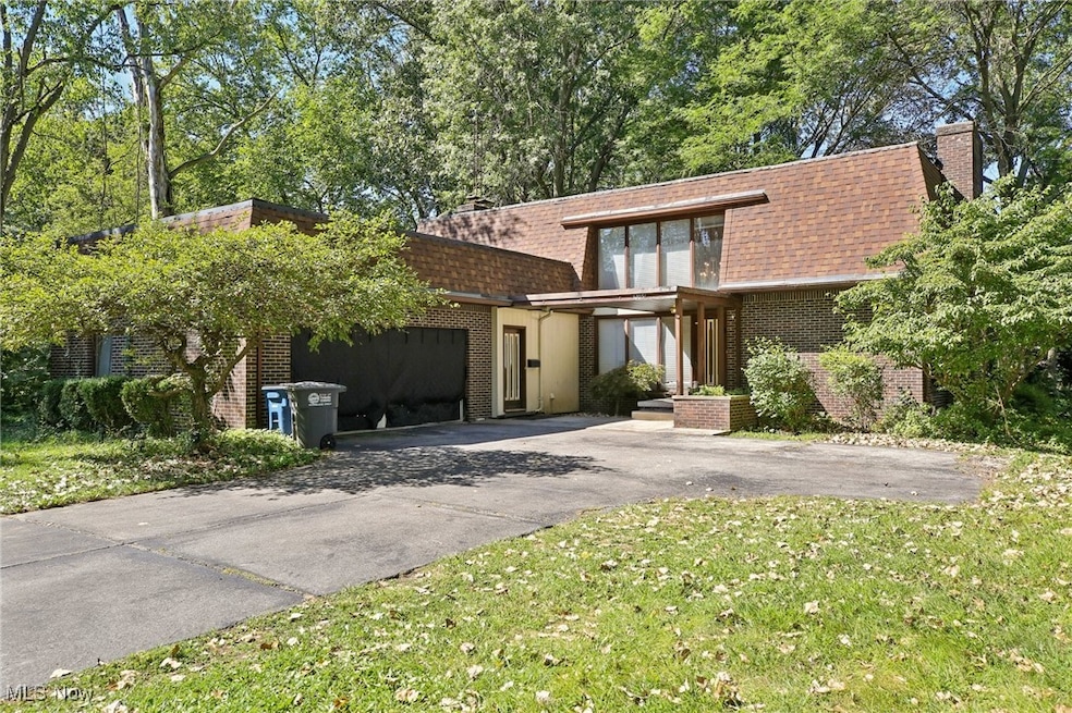 View of front of home featuring driveway, brick siding, a shingled roof, mansard roof, and a garage