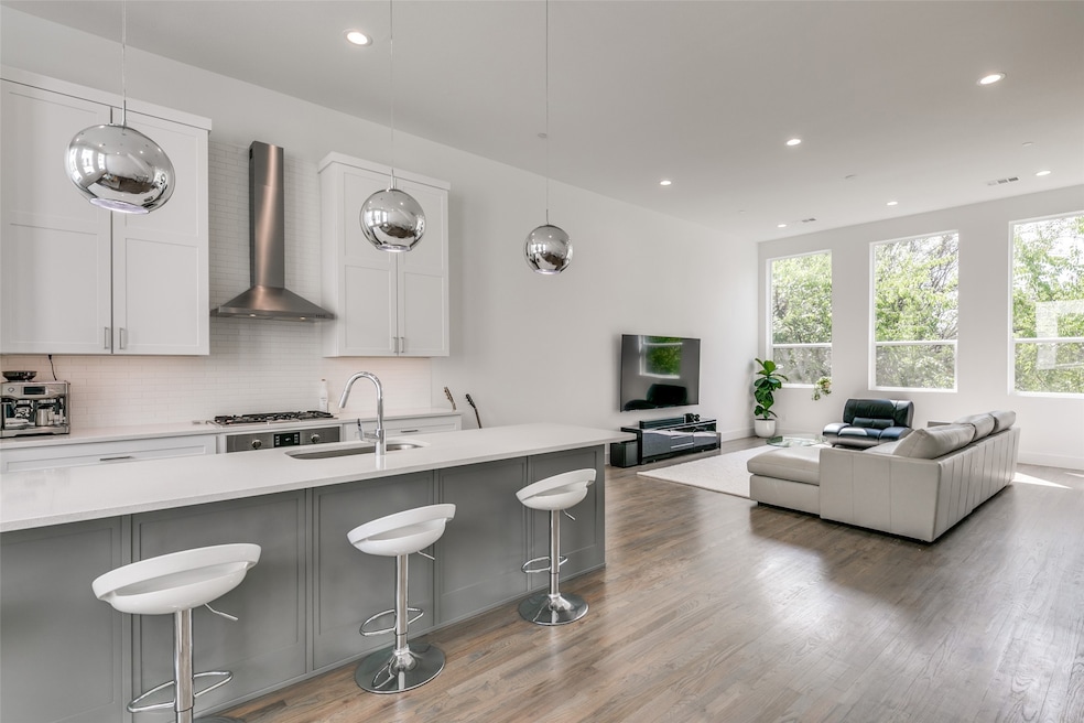 Kitchen featuring a kitchen breakfast bar, white cabinetry, hanging light fixtures, backsplash, and wall chimney exhaust hood