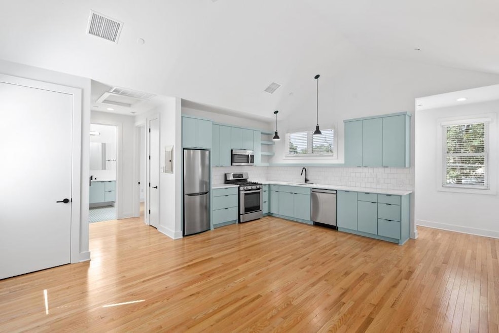 Kitchen featuring light wood-type flooring, light countertops, open shelves, pendant lighting, and stainless steel appliances