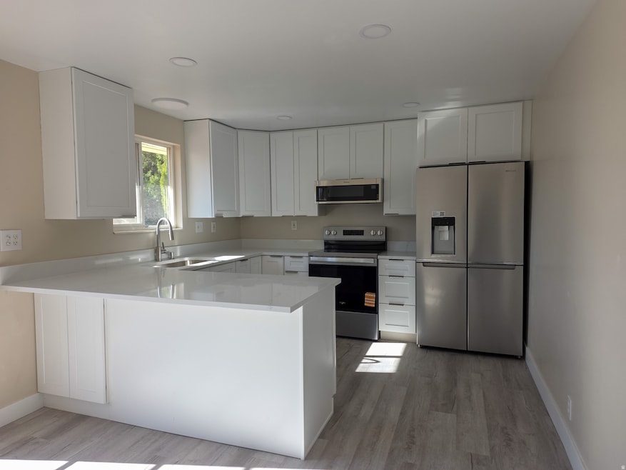 Brand new Kitchen featuring new stainless steel appliances, a peninsula, white cabinetry, light stone countertops, and light wood-style flooring 11/2/2025.