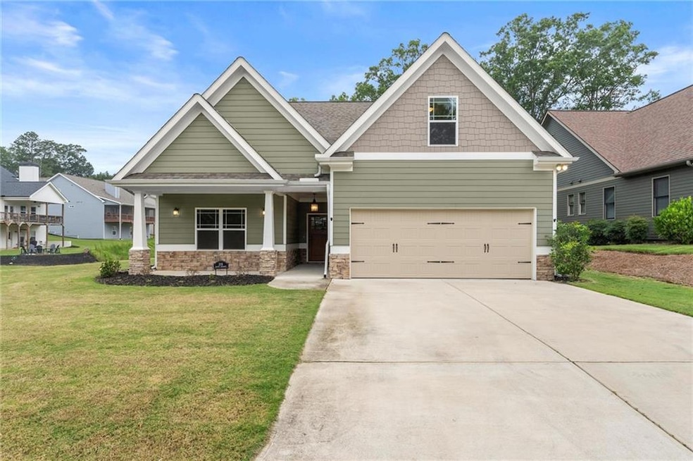 Craftsman house with stone siding, a front lawn, concrete driveway, a garage, and covered porch