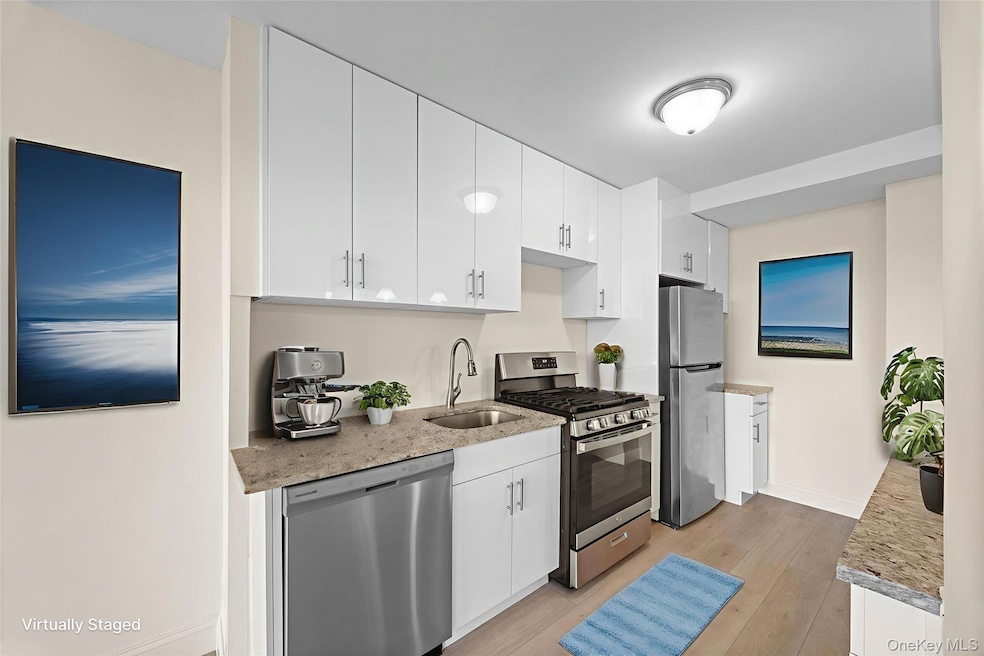 Kitchen with appliances with stainless steel finishes, light stone countertops, and white cabinetry