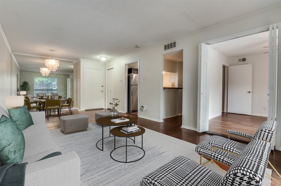 Living room featuring ornamental molding, wood finished floors, a chandelier, and a textured ceiling