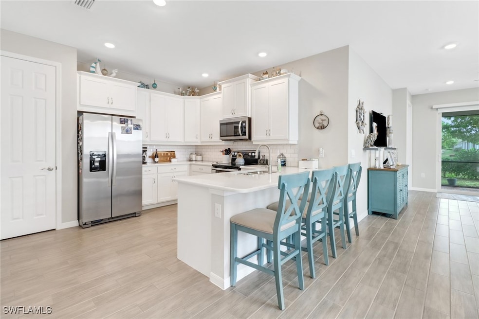 Kitchen with kitchen peninsula, stainless steel appliances, white cabinetry, and a breakfast bar area