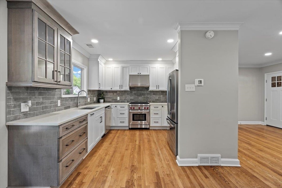 Kitchen with appliances with stainless steel finishes, under cabinet range hood, a sink, crown molding, and light countertops