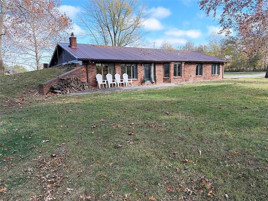 View of front of house featuring a patio, a front lawn, brick siding, a chimney, and a metal roof