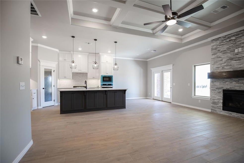 Kitchen with a stone fireplace, coffered ceiling, black microwave, decorative light fixtures, and a kitchen island with sink