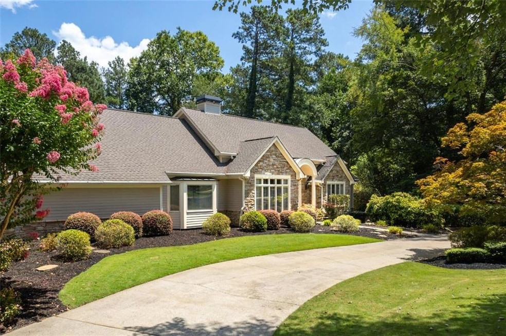 View of front of property featuring stone siding, roof with shingles, a chimney, a front yard, and view of scattered trees