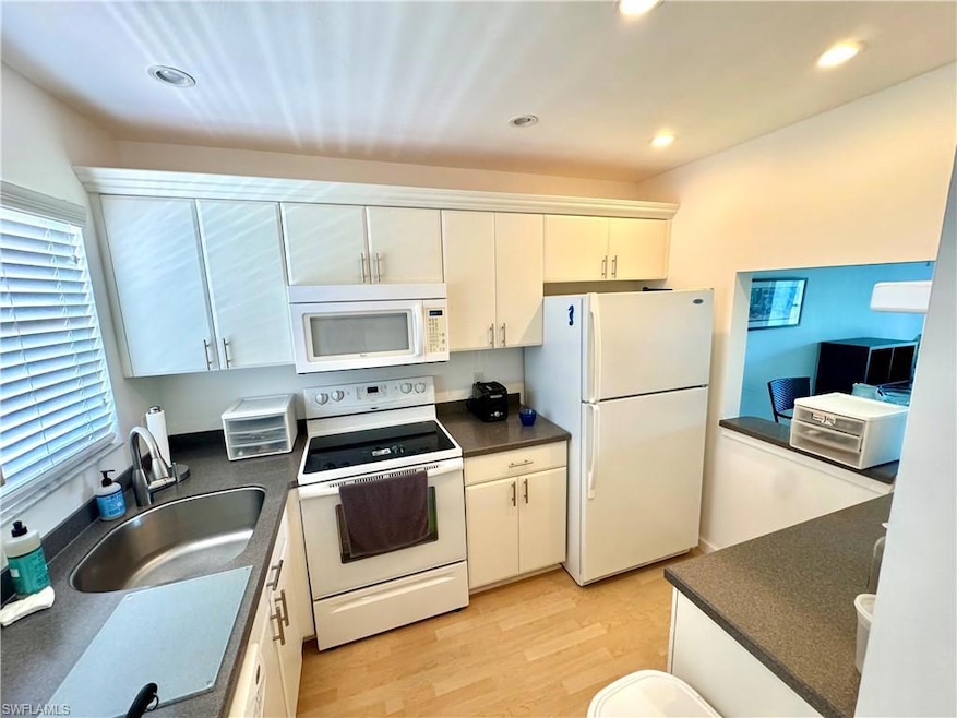 Kitchen featuring white appliances, dark countertops, light wood finished floors, recessed lighting, and white cabinets