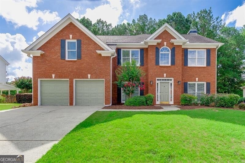 Colonial home with a garage, brick siding, concrete driveway, and a front lawn