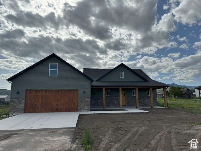 View of front of home with stone siding, driveway, covered porch, and a garage