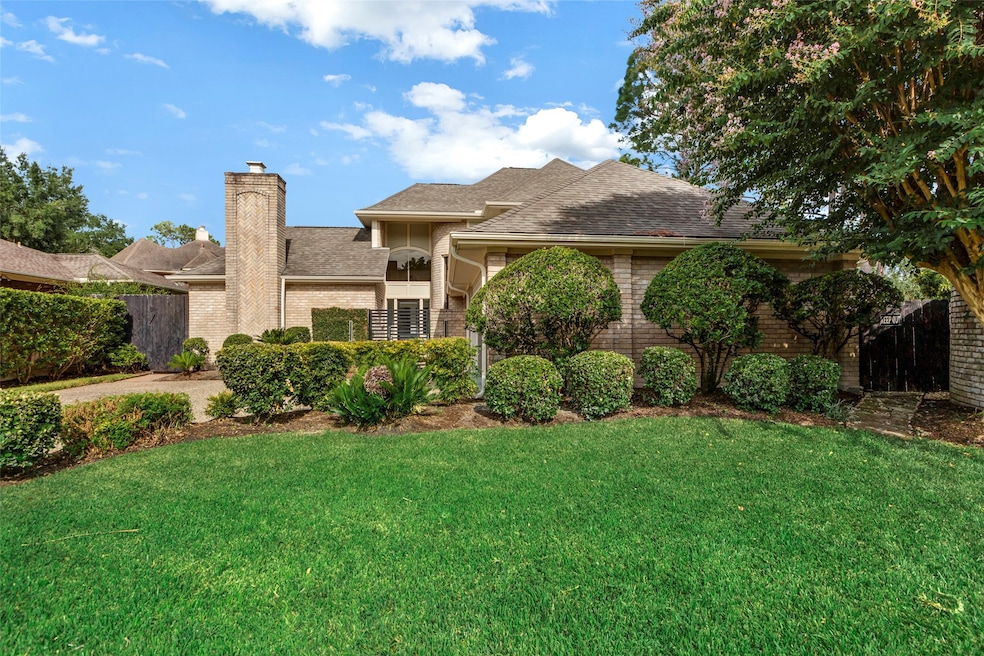 This charming home features a well-maintained brick exterior, a prominent chimney, and lush landscaping with manicured bushes and trees, offering great curb appeal in a serene neighborhood setting.