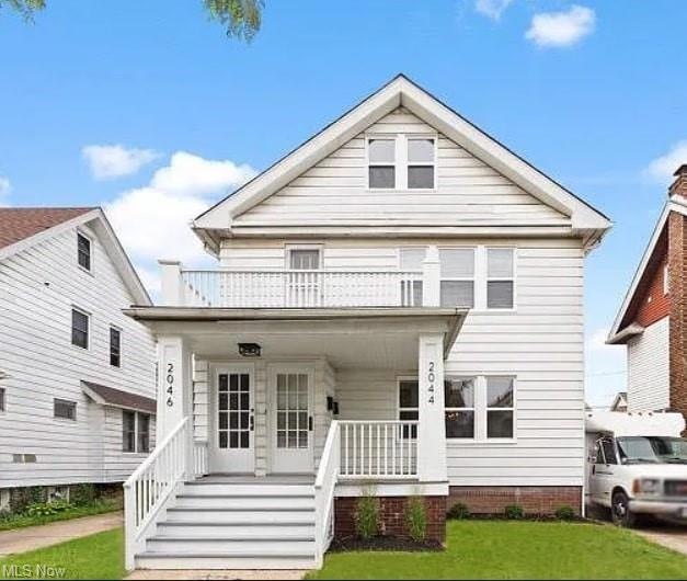 View of front of home with a front yard, a porch, and balcony
