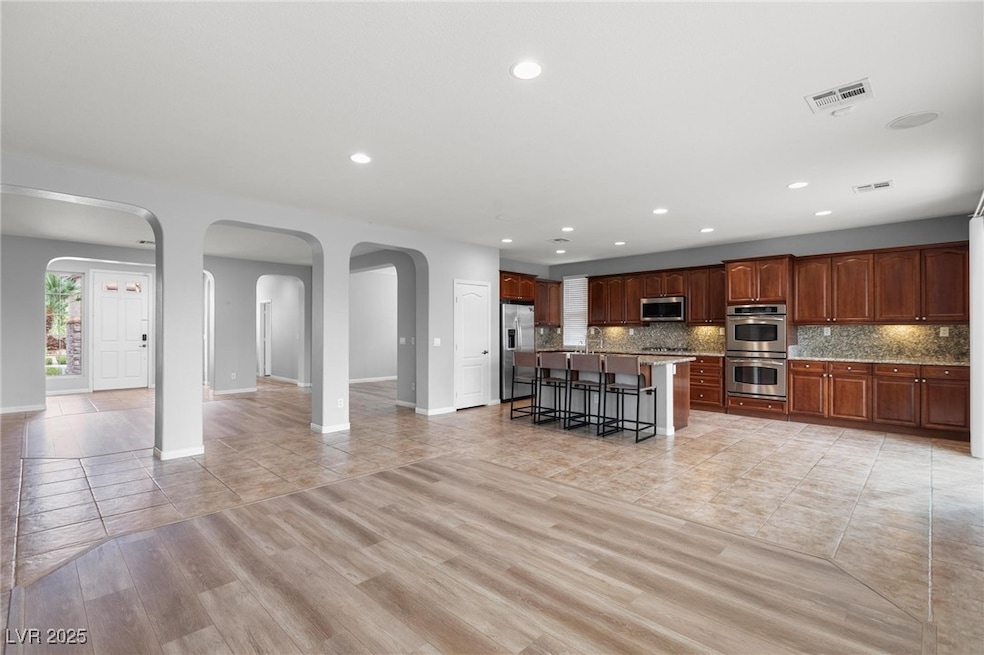 Kitchen featuring open floor plan, a breakfast bar, an island with sink, decorative backsplash, and light tile patterned floors