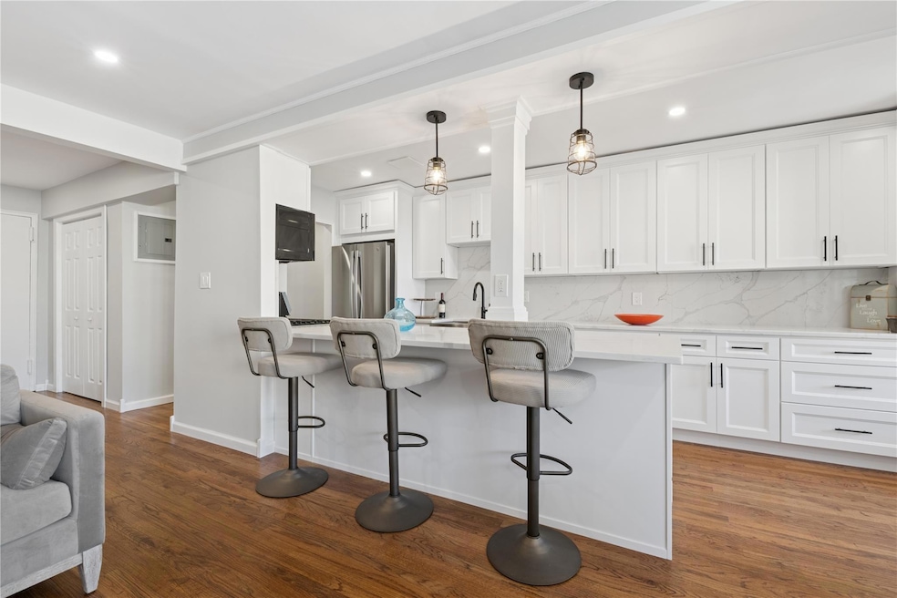Kitchen featuring a breakfast bar, tasteful backsplash, white cabinets, light countertops, and freestanding refrigerator